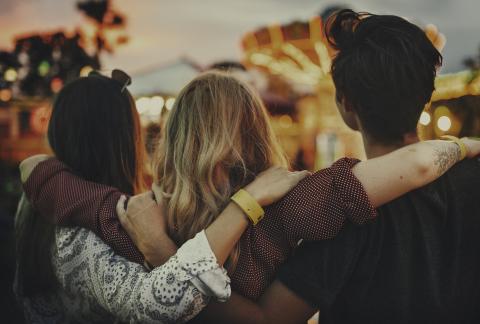 Back view of friends with arms around each other at a fair